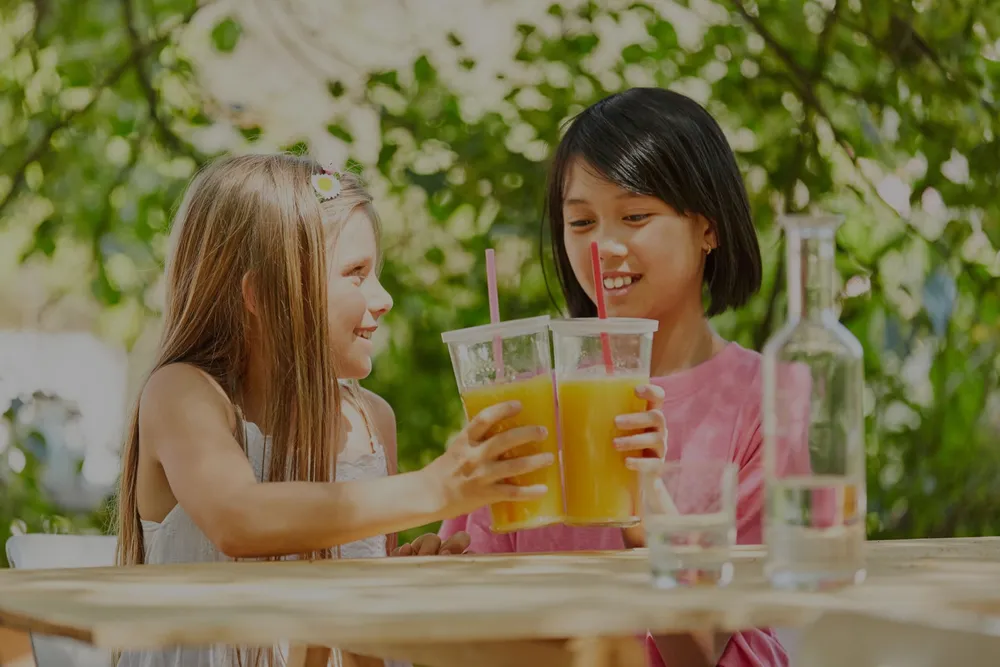 Two children sharing cold drinks at an outdoor table
