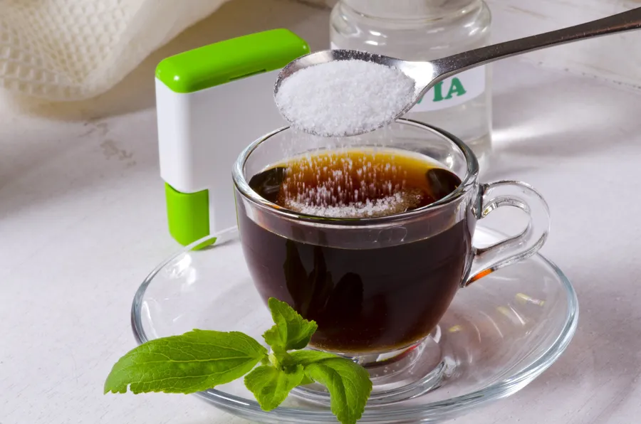 Granulated sweetener being spooned into a cup of tea